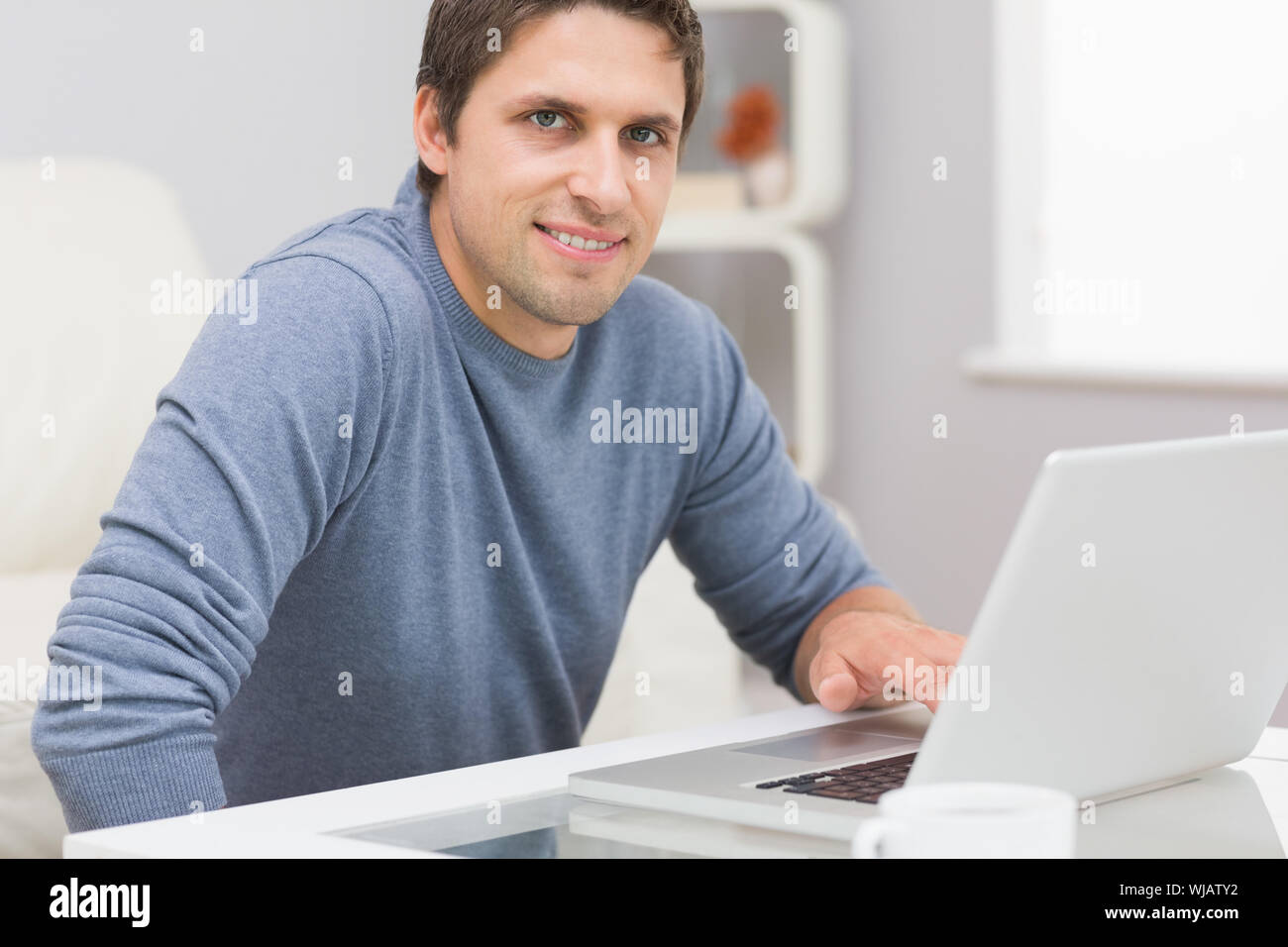 Portrait of smiling man using laptop in living room Stock Photo