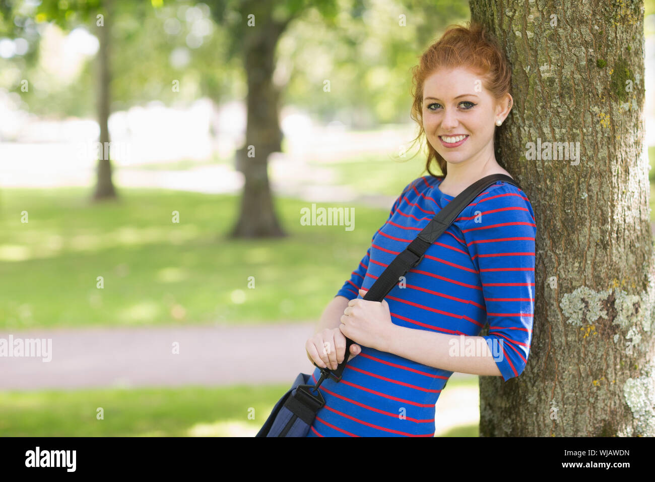 Cute redhead student leaning against a tree Stock Photo