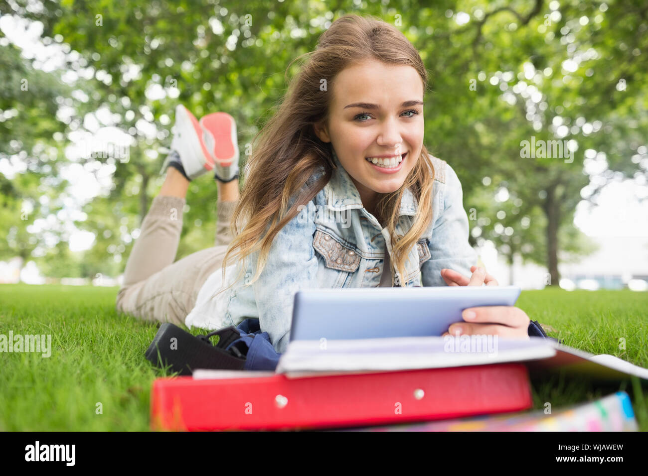 Smiling student lying on the grass studying with her tablet pc Stock Photo