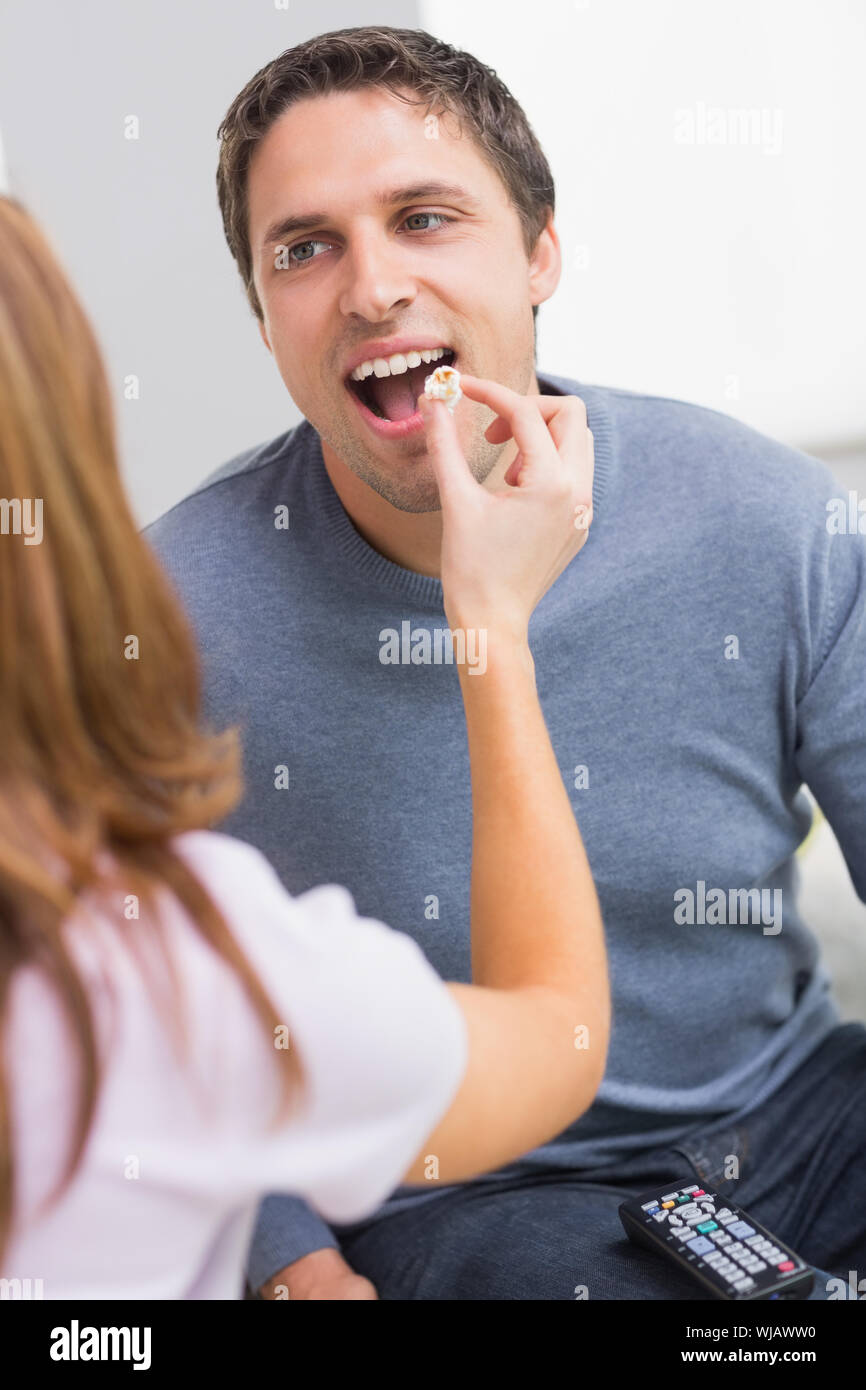 Cropped woman feeding popcorn to a happy man at home Stock Photo