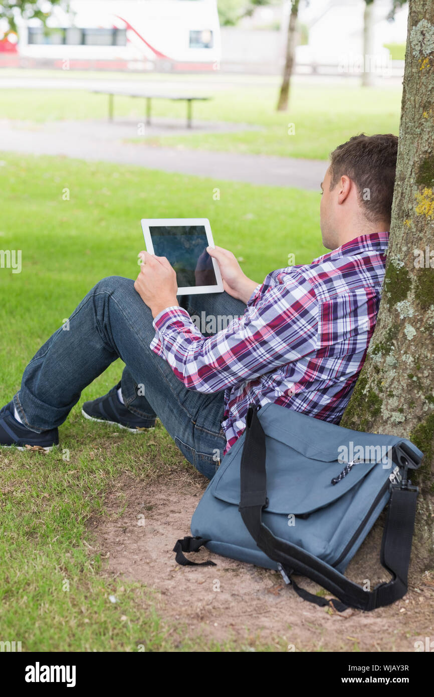 Student using his tablet pc outside leaning on tree Stock Photo