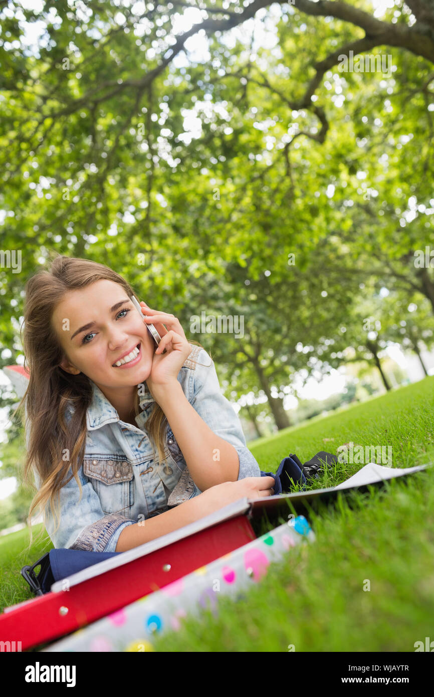 Young smiling student lying on the grass on the phone Stock Photo