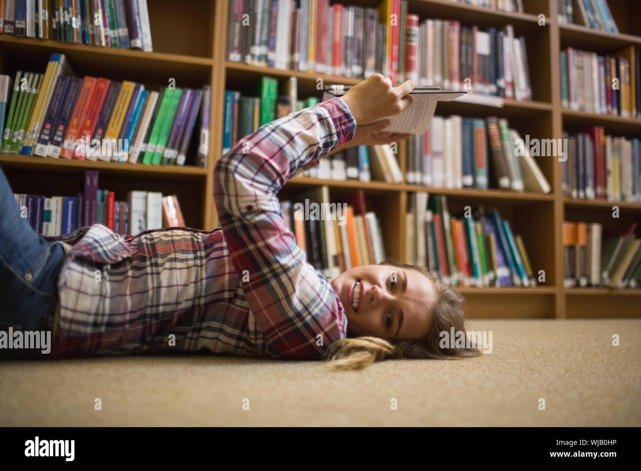 Pretty happy student lying on library floor reading book Stock Photo ...