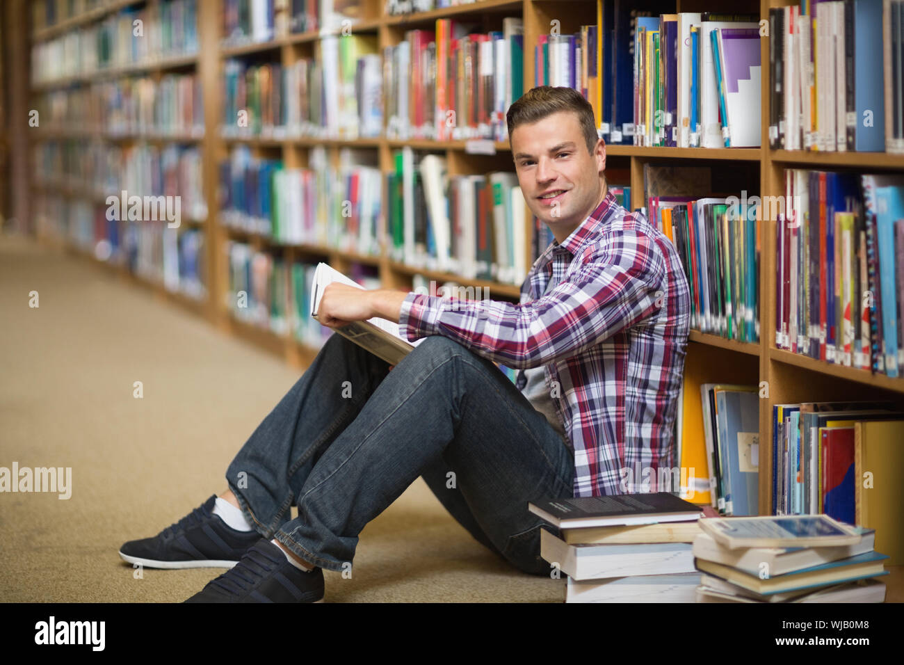 Happy student sitting on library floor reading Stock Photo