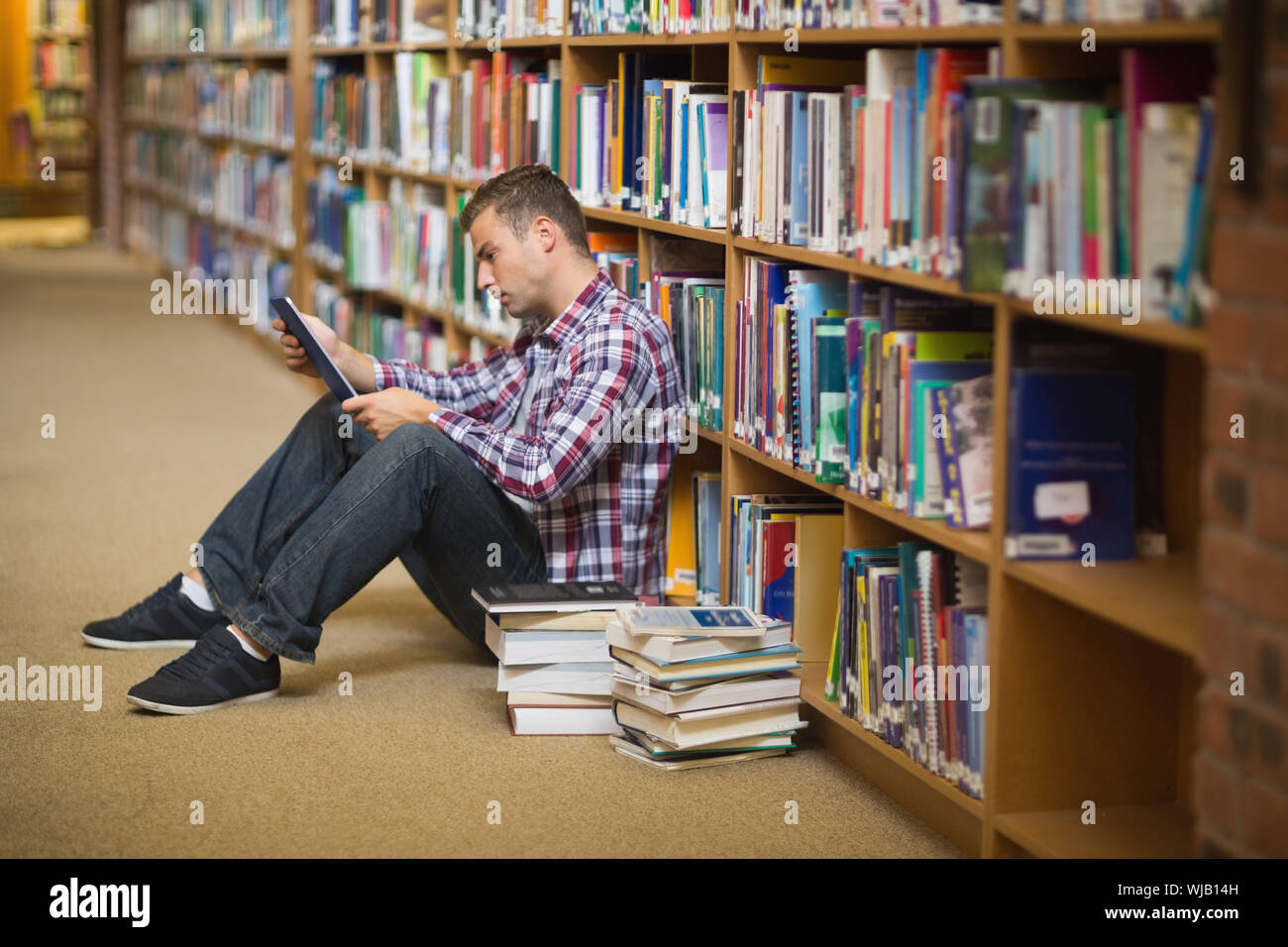 Focused young student sitting on library floor using tablet Stock Photo