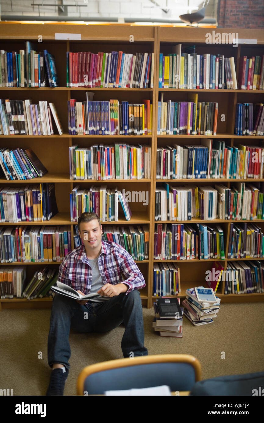 Happy young student sitting on library floor reading Stock Photo