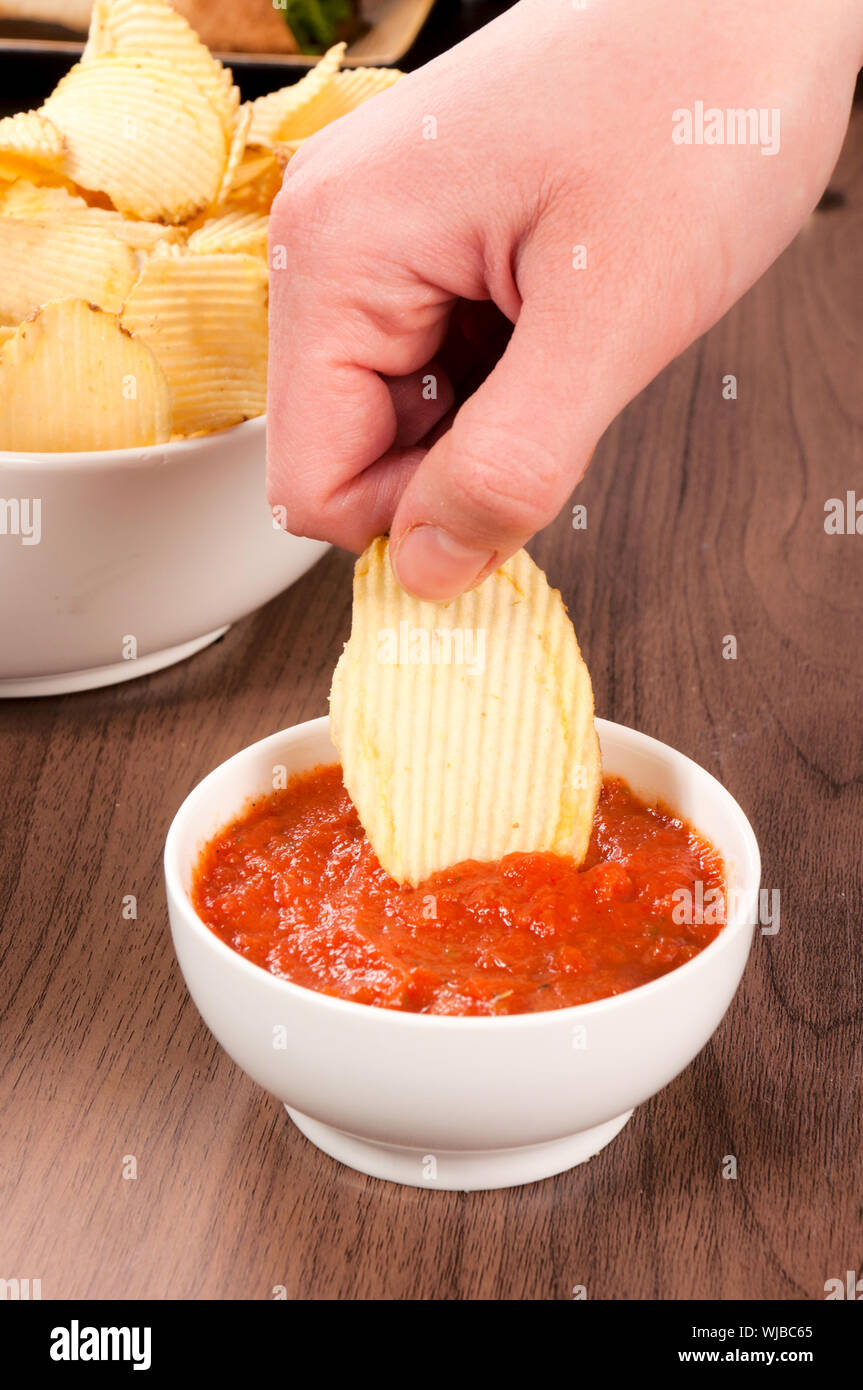 Hand dipper potato chips in the salsa sauce Stock Photo Alamy