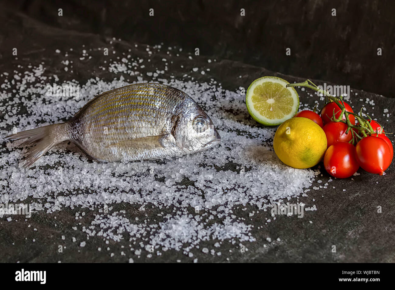 raw mediterranean dorado is a good italian fish with ingredients for cooking: raw tomatoes and lemon Stock Photo