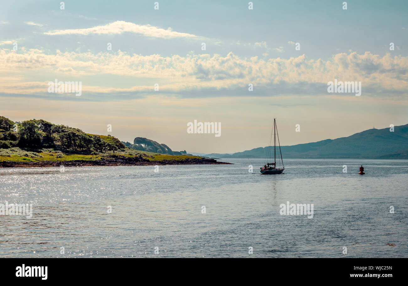 A sail boat leaves Loch Aline behind. Loch Aline is a small salt water loch home to fish, birds and game, located in Morvern, Lochaber, Scotland. Stock Photo
