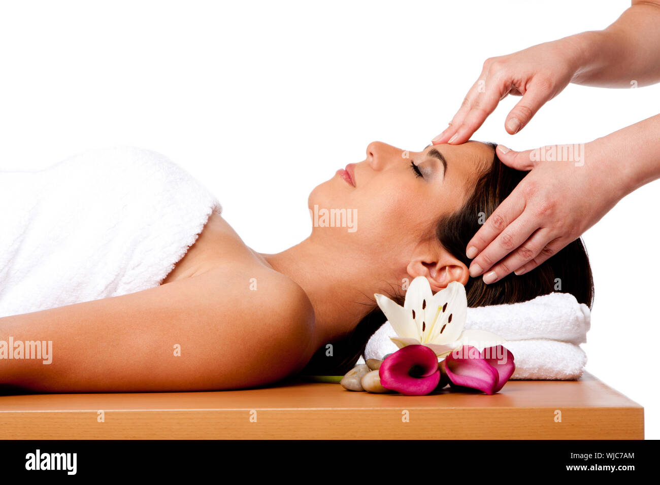Beautiful happy peaceful sleeping woman at a spa, laying on wooden massage table with head on pillow wearing a towel getting a facial massage, isolate Stock Photo