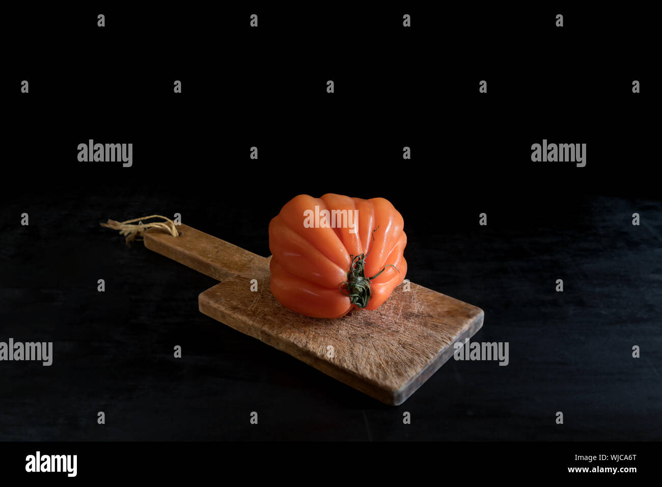 Colorful juicy ugly tomato on wooden cutting board on a black backgound, rustic style and low key with copy space Stock Photo
