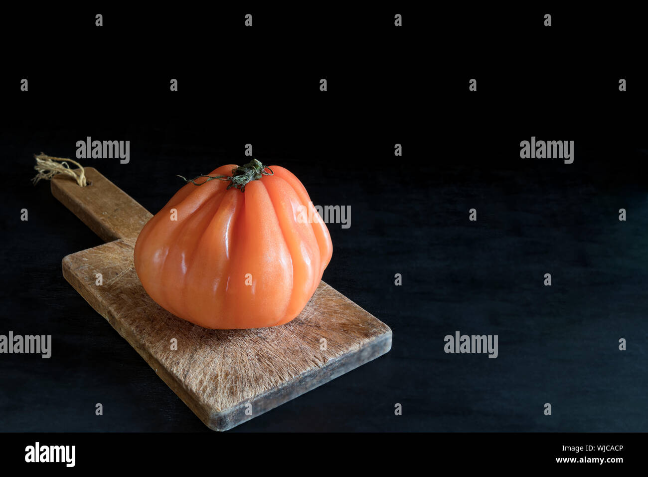 Colorful juicy ugly tomato on wooden cutting board on a black backgound, rustic style and low key with copy space Stock Photo