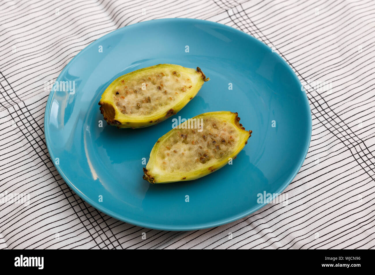 View of two halves of a yellow indian fig (also called prickly pear) on a blue plate. Stock Photo