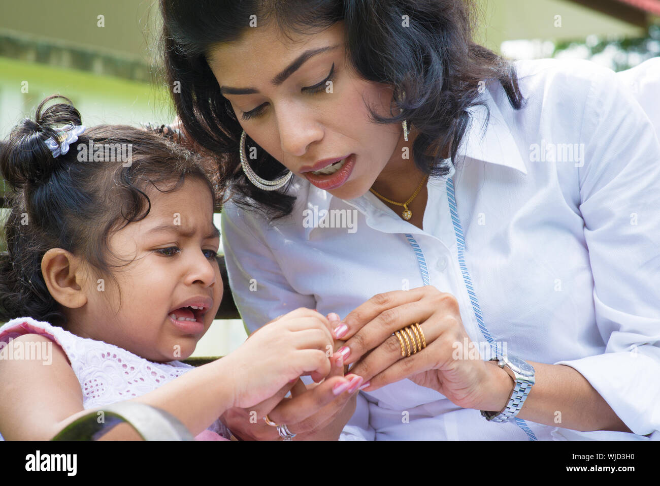 Indian family outdoor. Mother is comforting her crying daughter with injured finger. Stock Photo