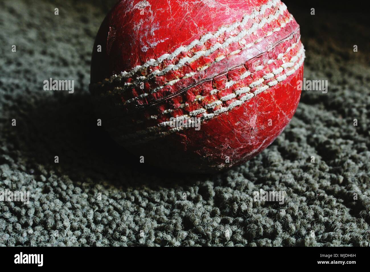 Close-up Of Red Cricket Ball On Rug At Home Stock Photo
