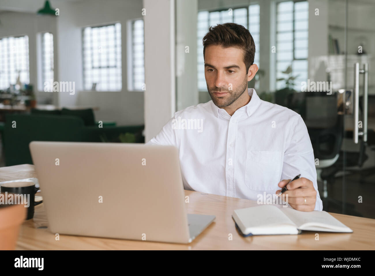 Young businessman writing down notes while working on a laptop Stock Photo
