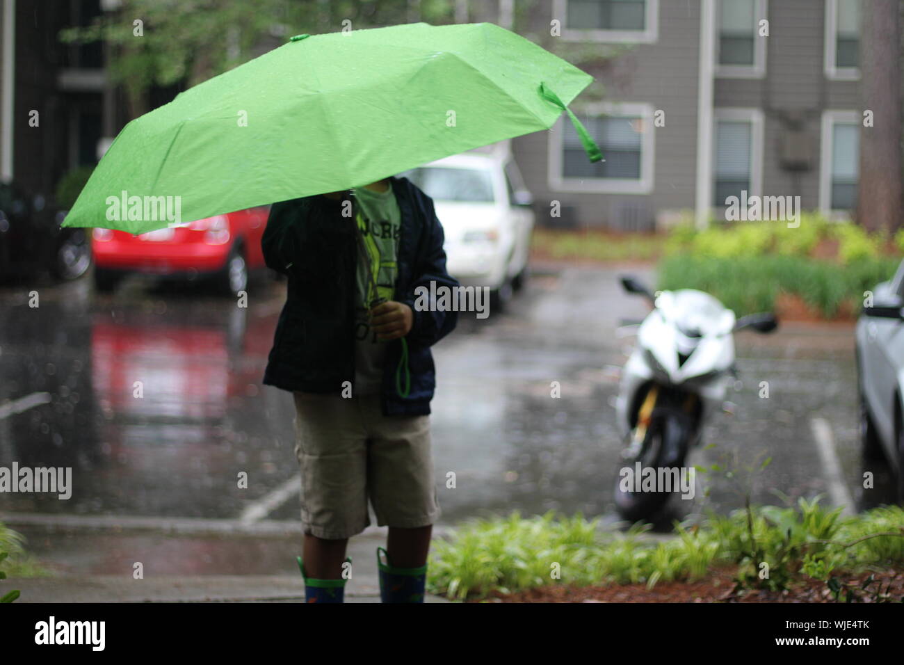 Midsection Of Boy With Umbrella Standing On Street During Rainfall Stock Photo