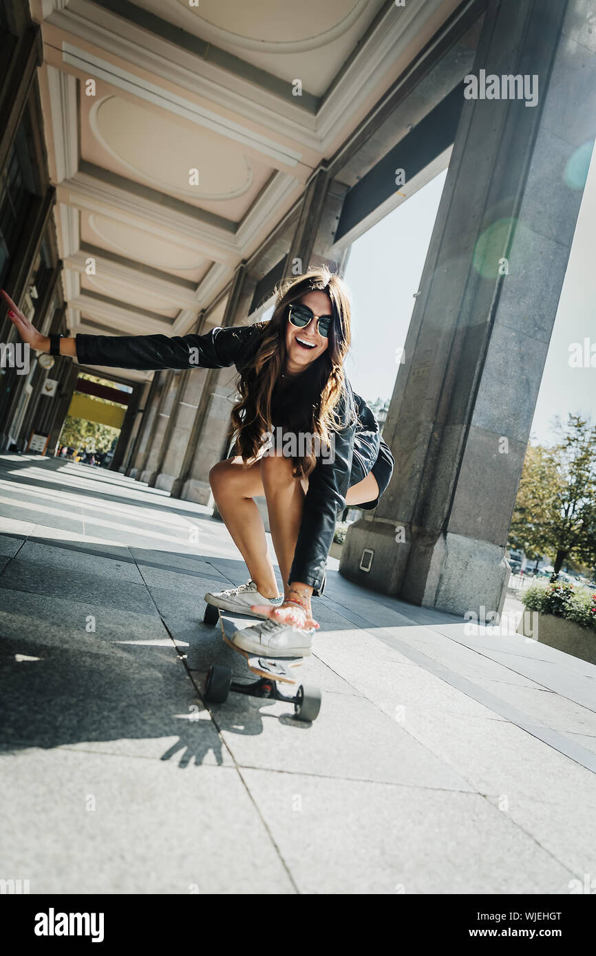 Beautiful young skater woman riding on her longboard in the city. Stylish girl in street clothes rides on a longboard. Skateboard, street photo, life Stock Photo