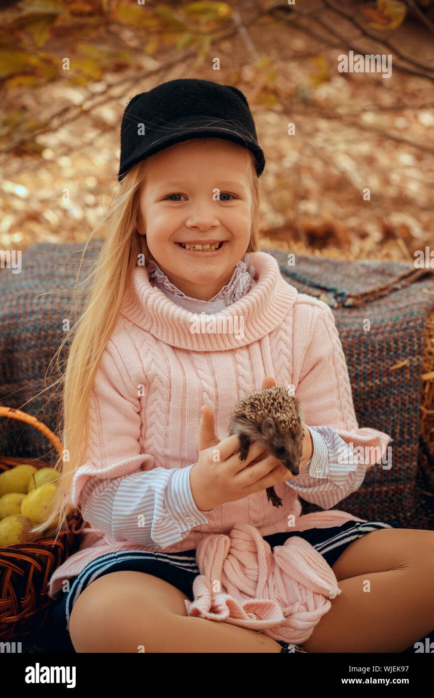 beautiful small girl with cute and funny hedgehog baby in autumn