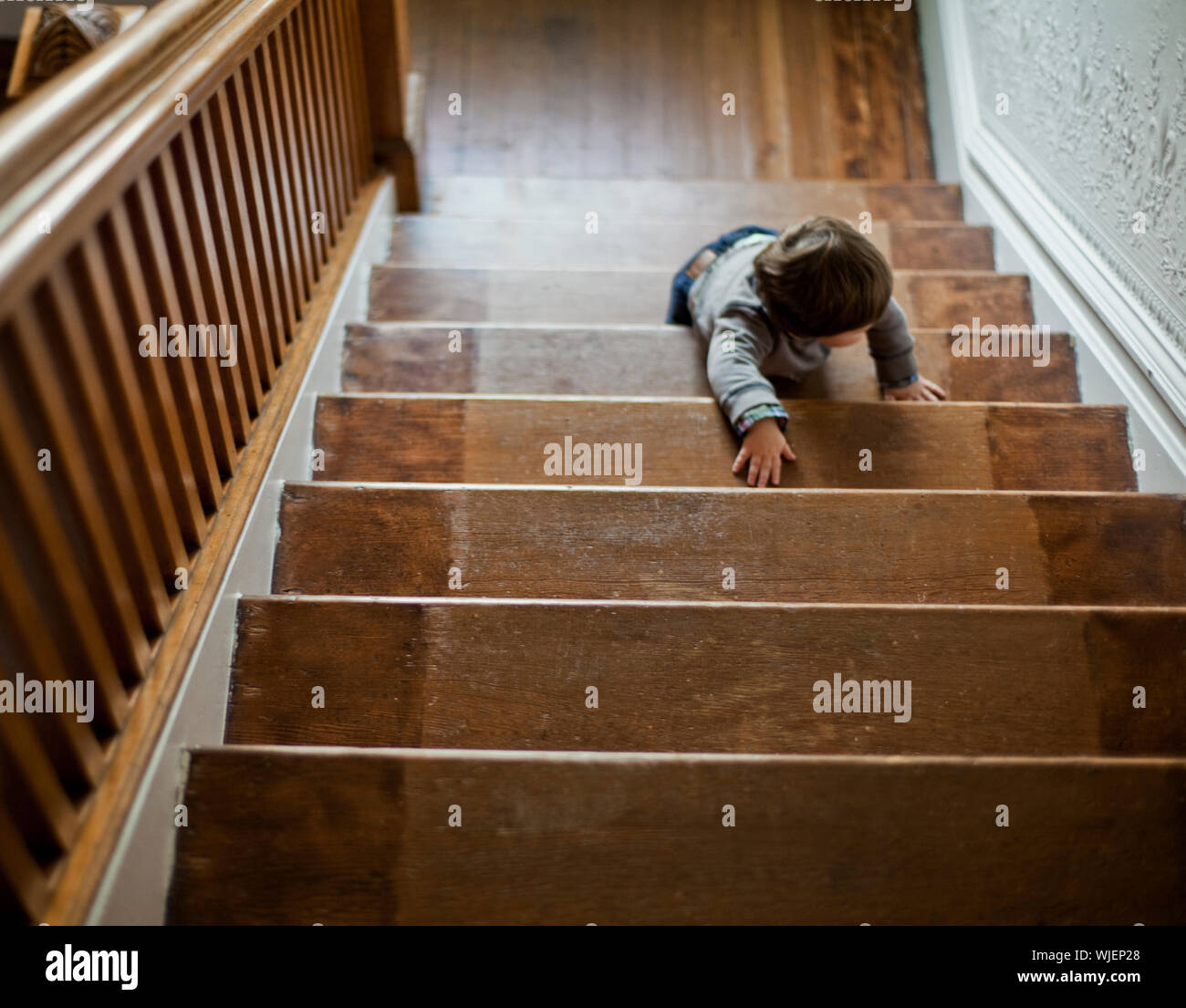 Toddler climbing up a wooden staircase. Stock Photo