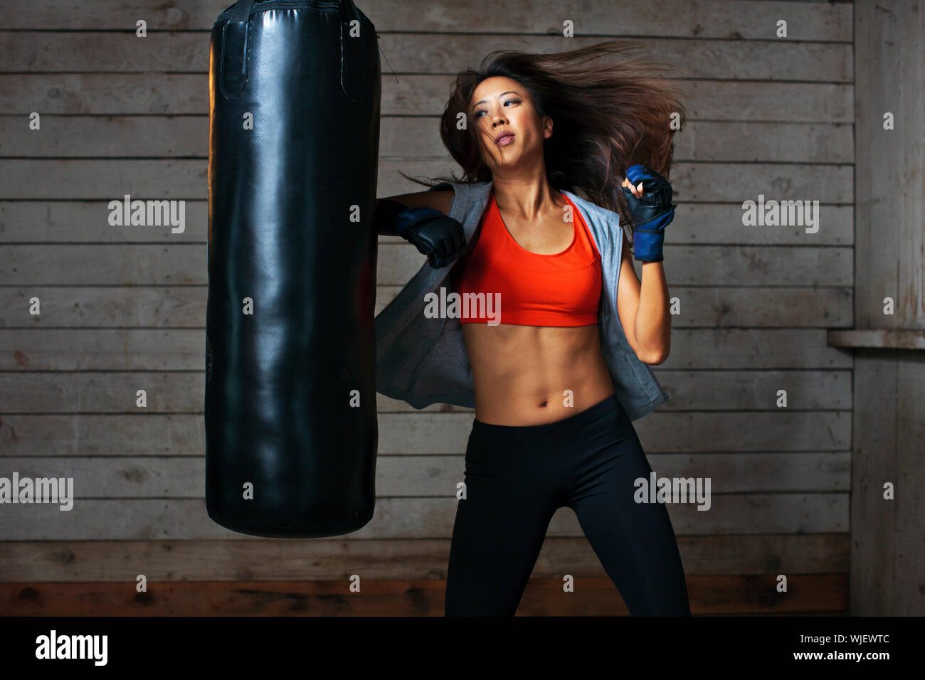 Tough young woman punching boxing bag. Stock Photo