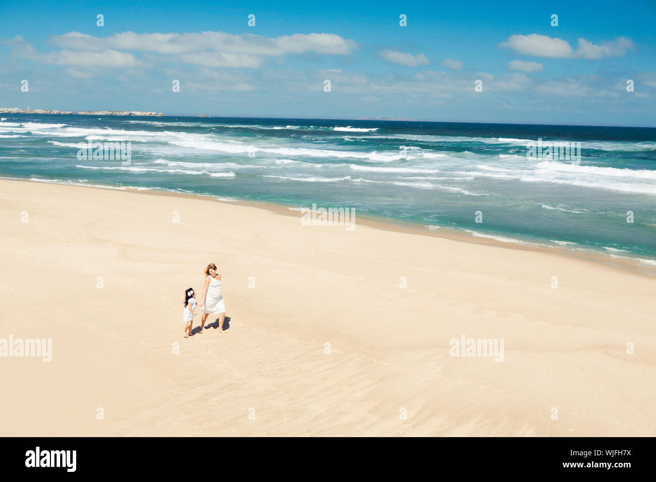 Beautiful woman and her little daughter walking on the beach Stock Photo. 