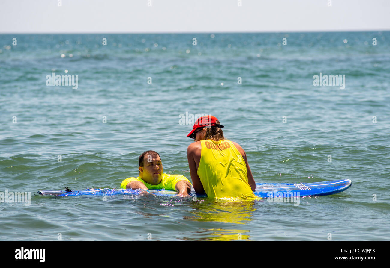 Lifeguard John Livingstone, 24 of Medford, New Jersey helps guide Anthony Tarquinio, 27, of Buena, New Jersey chat while resting on a paddle board dur Stock Photo