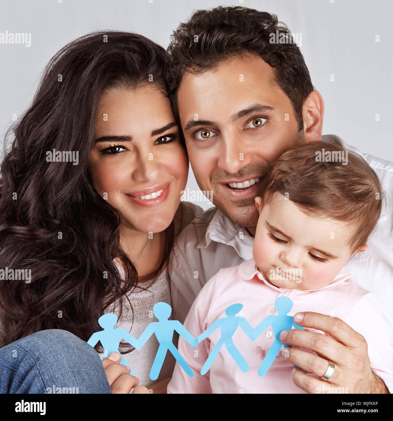 Beautiful family together isolated on gray background, happy young parents carry little daughter, people-shaped blue paper bonding toy in hands, toget Stock Photo