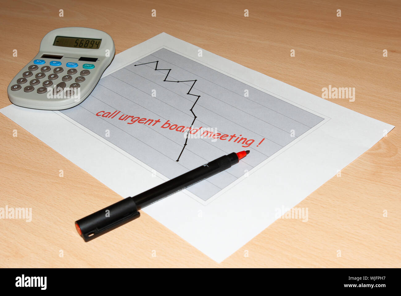 Graph of A4 paper showing a downward trend with 'Call urgent board meeting' written in red and pen and calculator beside Stock Photo