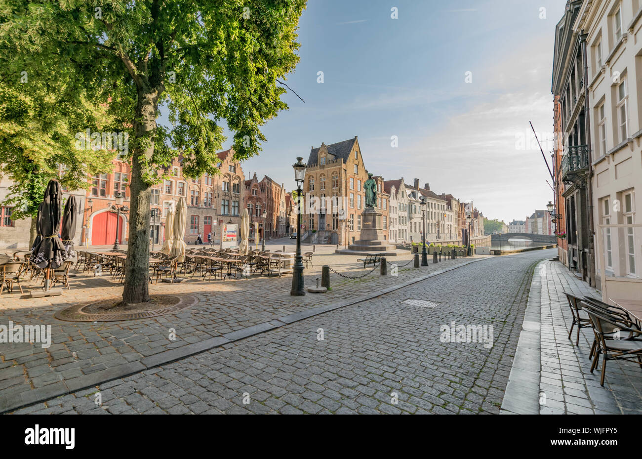 Cobblestone street, the Jan Van Eyck Monument and square, and rows of historic houses on either side of a canal in Bruges, Belgium Stock Photo