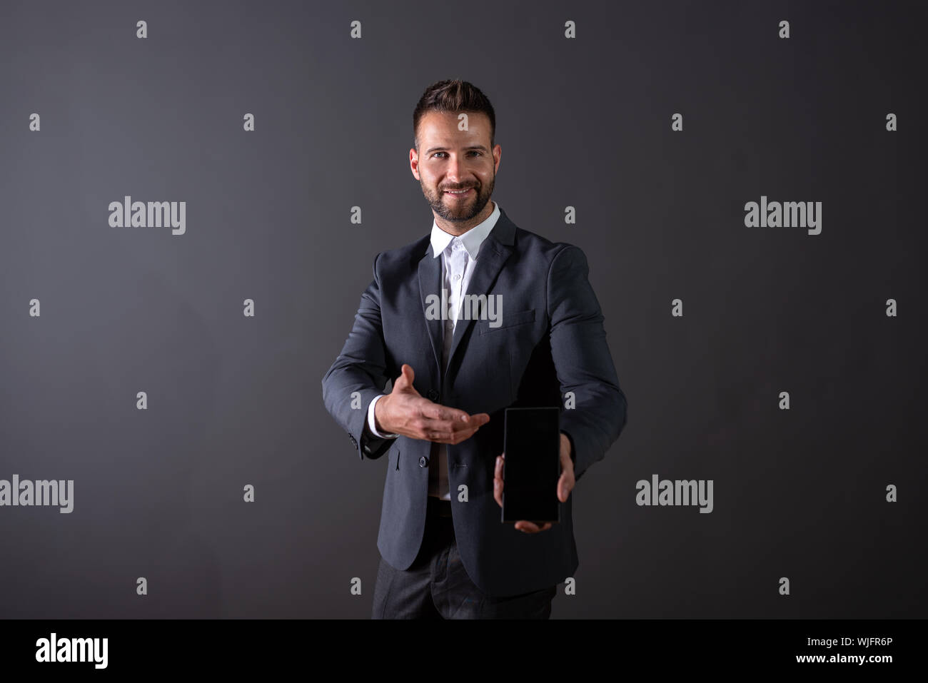 A smiling handsome young businessman in a suit showing the screen of a ...