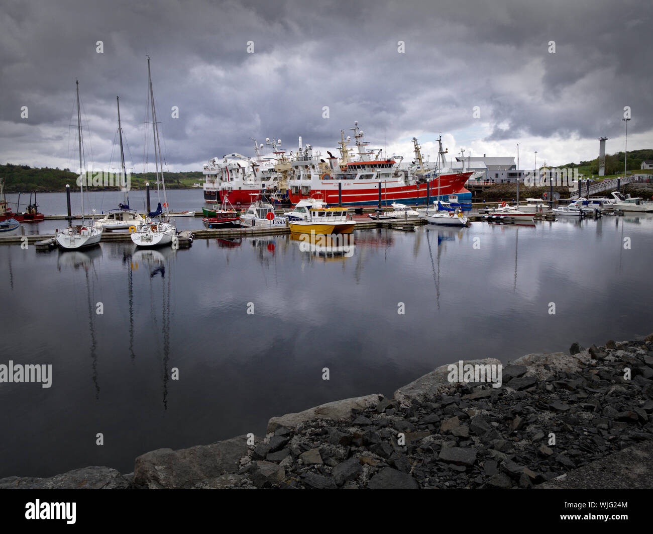 Killybegs, Co. Donegal, Ireland - May 19th, 2019 - Harbour with yachts, fishing vessels, overcast sky and stone quay in the foreground. Stock Photo