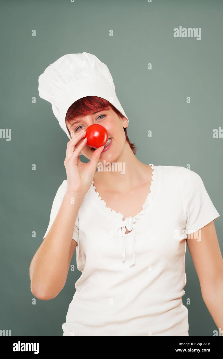 young female cook holding tomato on her nose Stock Photo