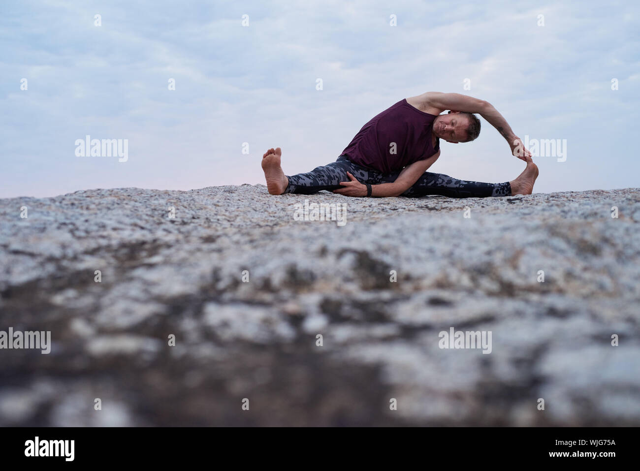 Man doing the revolved head to knee pose at dusk Stock Photo