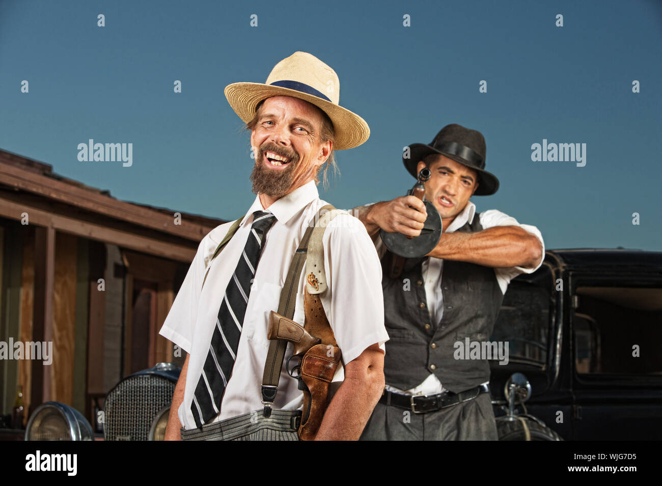 Easygoing vintage mobster with guard aiming gun Stock Photo