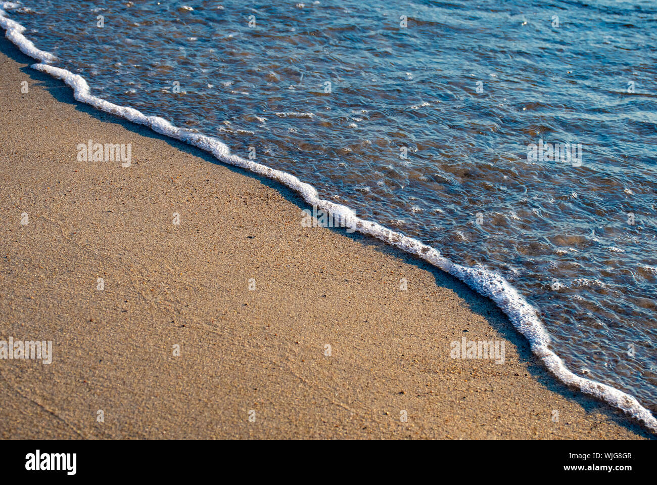 Small wave of the sea meets the sand on the shore of a sandy beach,  oblique line Stock Photo