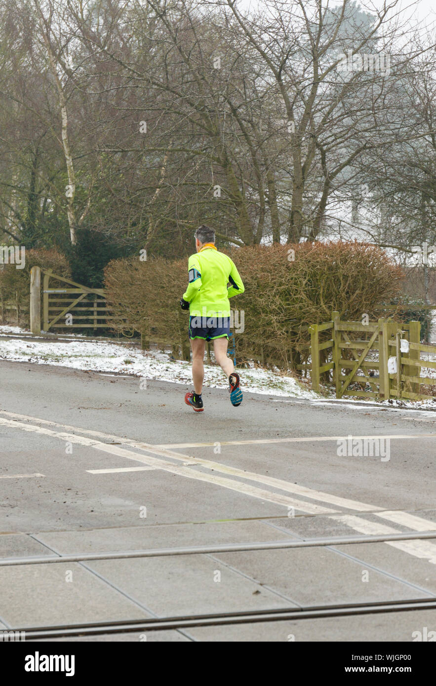 Male jogger running along the road in winter, dressed in high visibility clothing complete with an arm sports phone holder. England UK Stock Photo