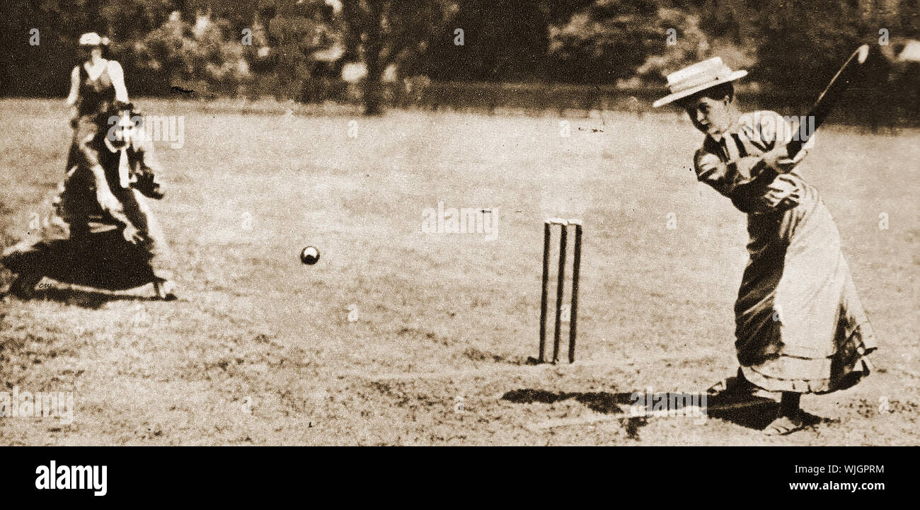 Women playing traditional sports in 1911 -  Females playing cricket in formal long dresses and hats. Stock Photo