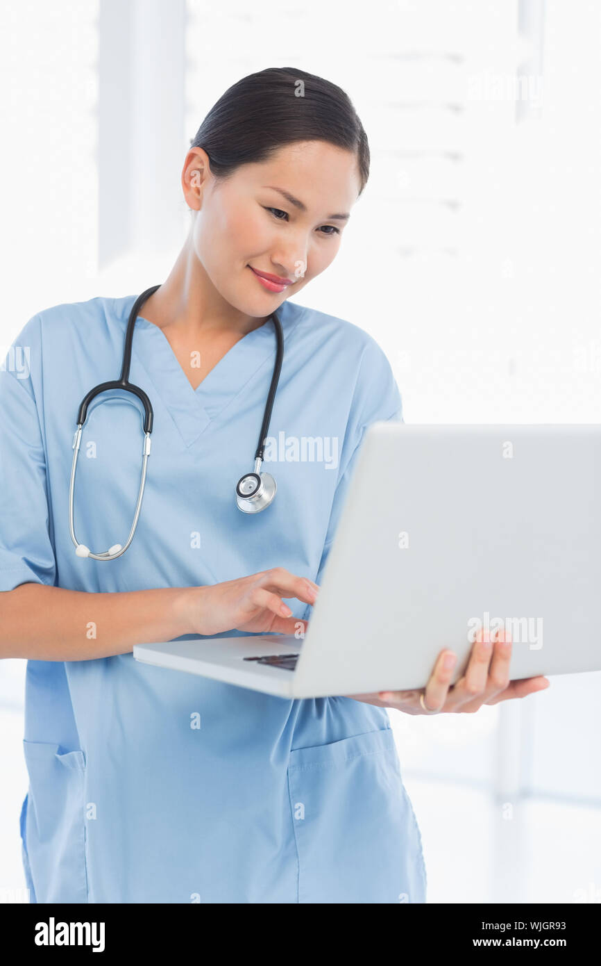 Concentrated female surgeon using a laptop in a bright hospital Stock Photo