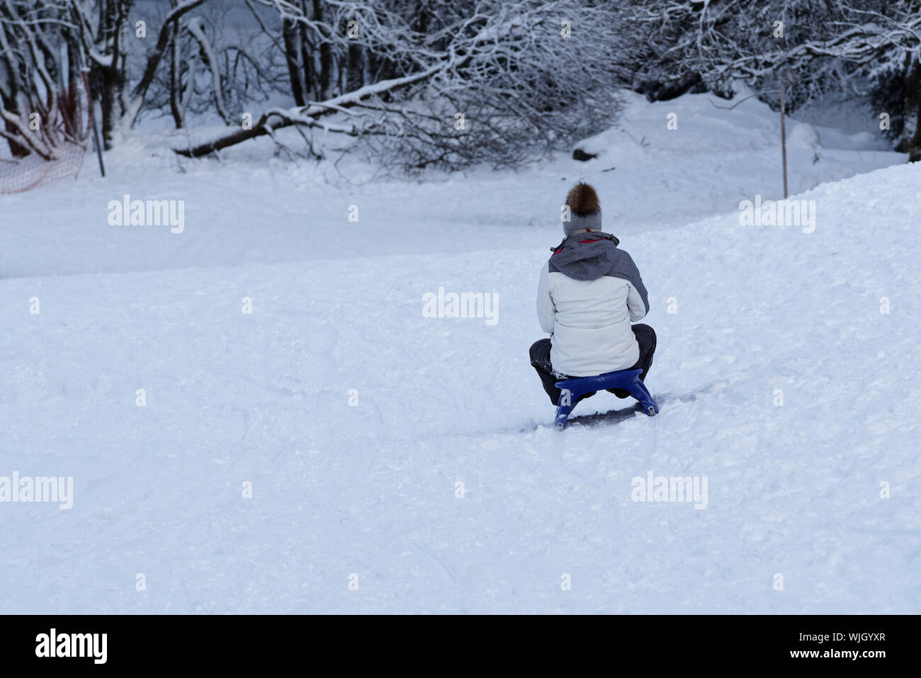 Young woman sledding on a sled by a toboggan run. Torfhaus resort in
