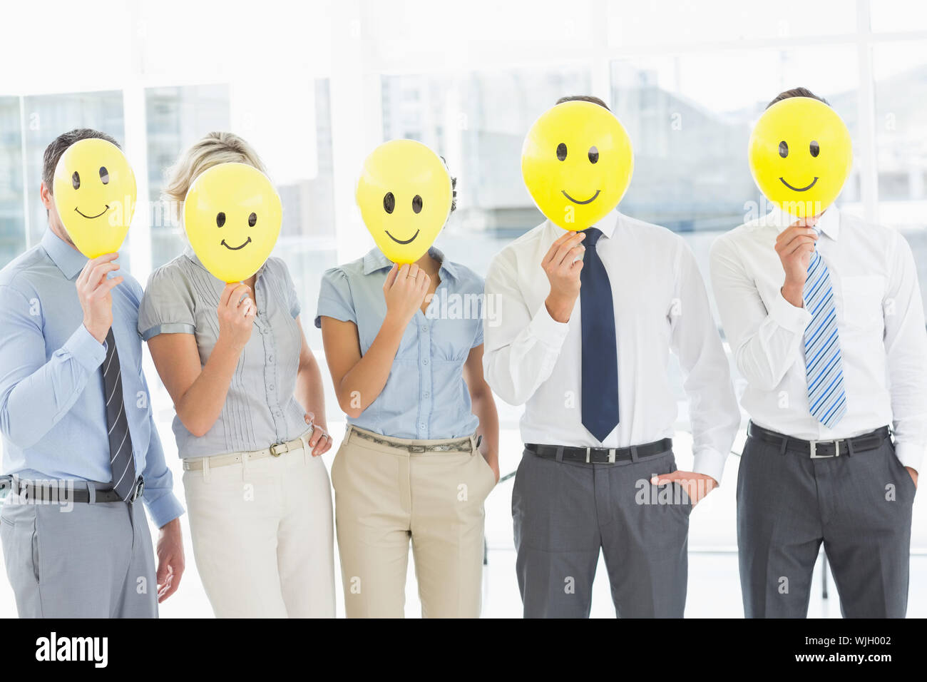 Group of business people holding happy smiles in front of their faces in a bright office Stock Photo
