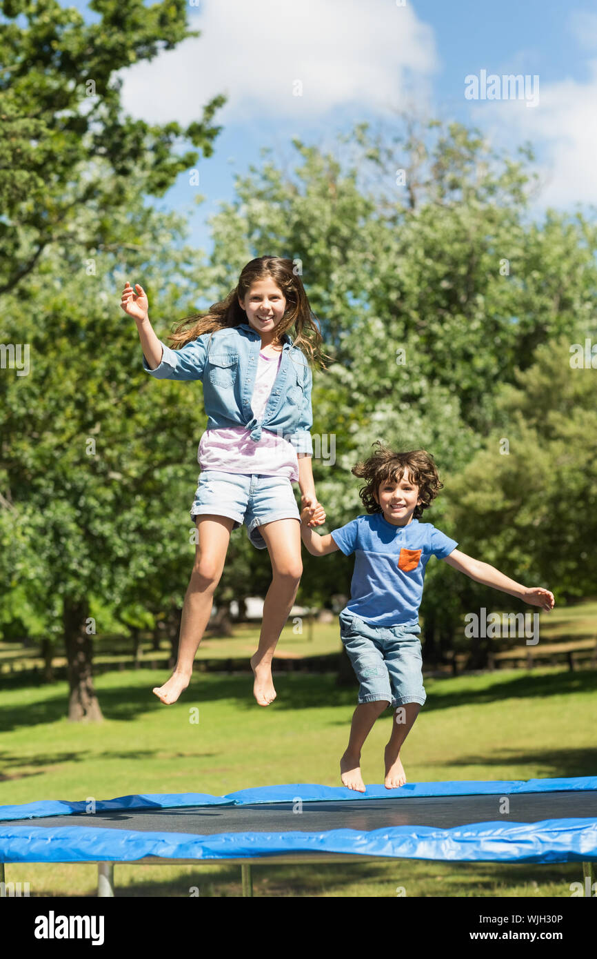 Full length of a happy boy and girl jumping high on trampoline in the ...