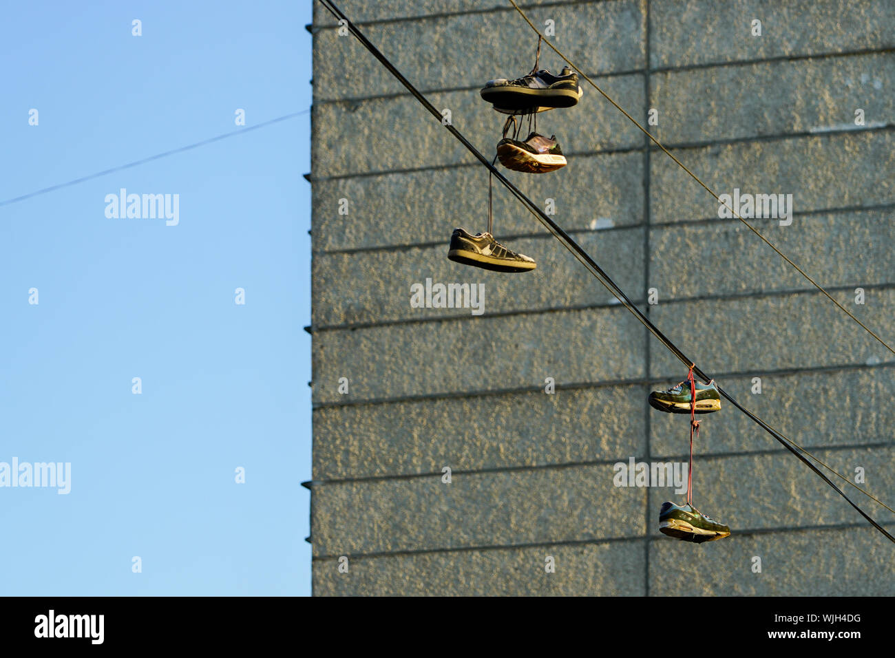 Several tennis shoes on power lines in front of a clear blue sky Stock