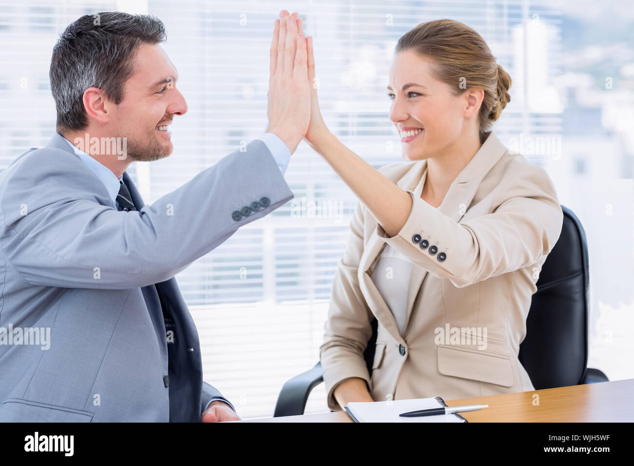 Smartly dressed young man and woman giving high five in a business ...