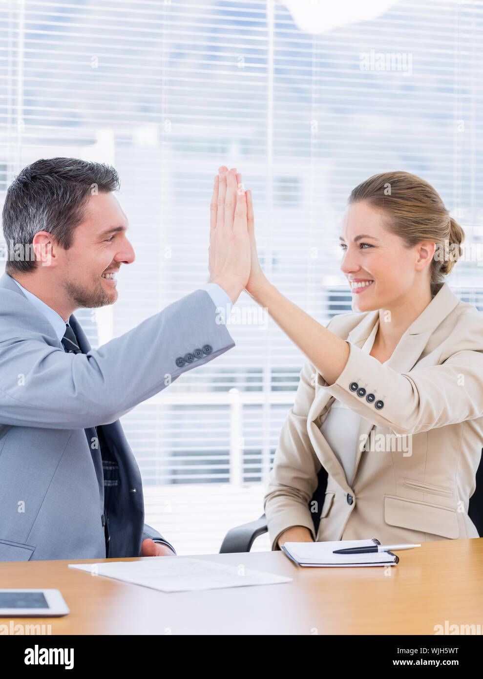 Smartly dressed young man and woman giving high five in a business ...