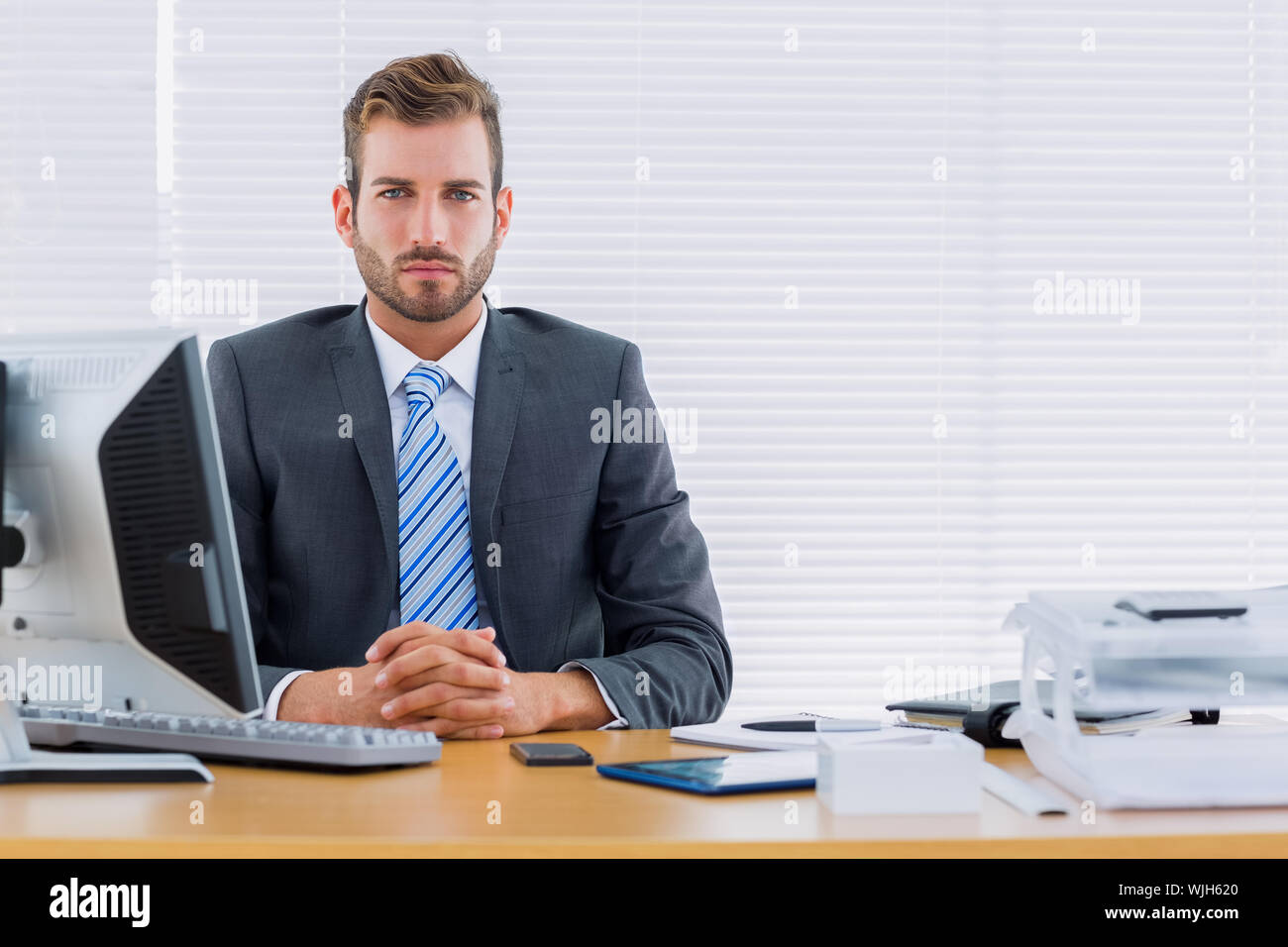 Portrait of a serious young businessman with computer at office desk ...