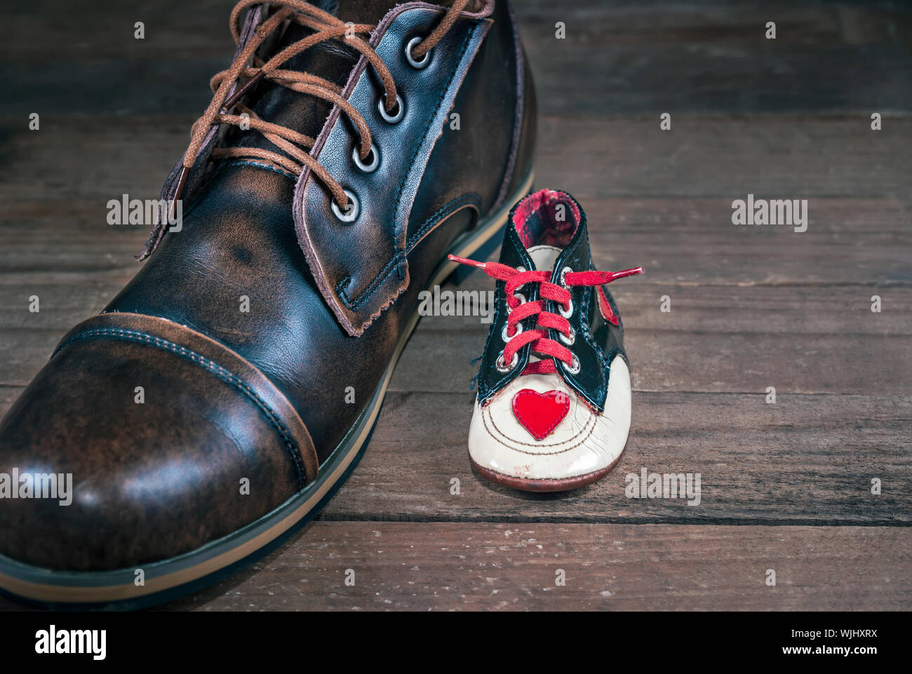 Newborn's shoe next to the same person's adult shoe. Concept image of growth, aging and evolution of fashion and design. Stock Photo