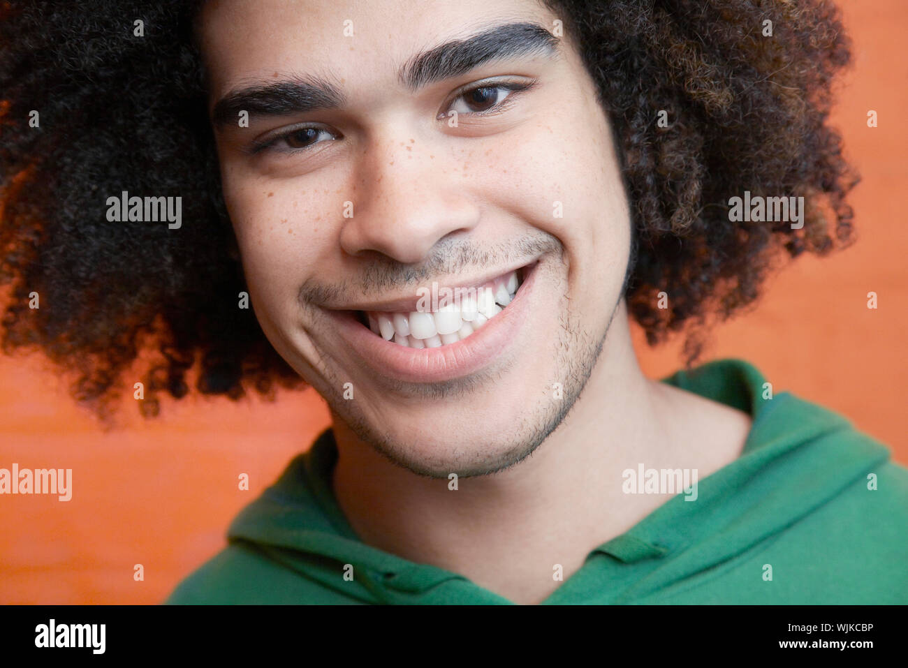 Closeup of smiling young man in front of orange wall Stock Photo - Alamy