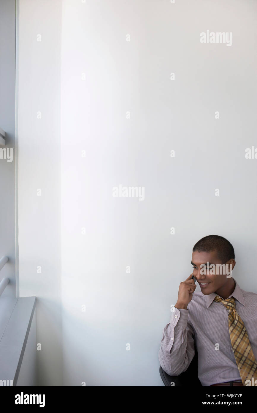 Smiling mixed race businessman using mobile phone in office against the wall Stock Photo