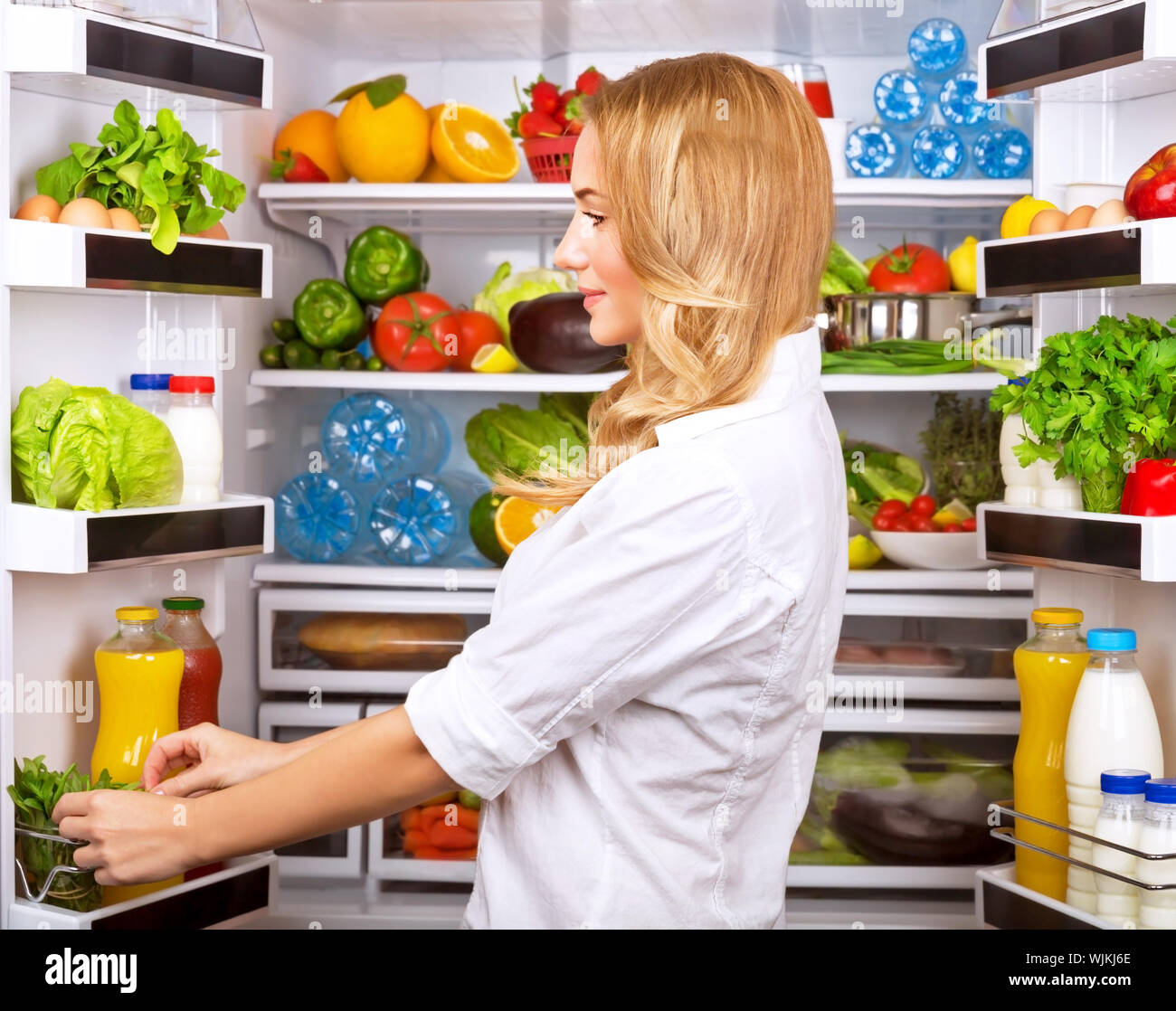 Happy female search something in the fridge, fresh fruits and vegetables in the refrigerator, cooking diet food, fit and body care concept Stock Photo